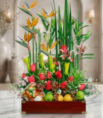 Arreglo floral Akebia con aves del paraíso, rosas rojas, lirios, orquídeas y frutas frescas sobre mármol, fondo de floristerí