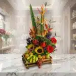 Arreglo floral exótico 'Bahamas' con aves del paraíso, girasoles, gerberas rojas y una base de frutas frescas como manzanas,