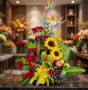 Impresionante arreglo floral con rosas rojas, girasoles vibrantes, aves del paraíso y frutas exóticas como manzanas, uvas y d