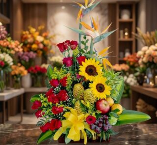 Impresionante arreglo floral con rosas rojas, girasoles vibrantes, aves del paraíso y frutas exóticas como manzanas, uvas y d