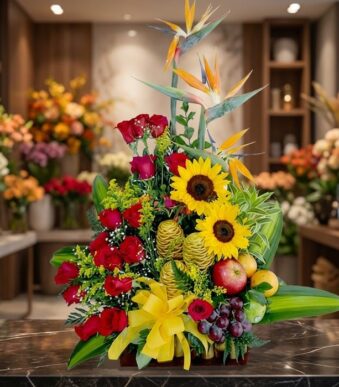 Impresionante arreglo floral con rosas rojas, girasoles vibrantes, aves del paraíso y frutas exóticas como manzanas, uvas y d