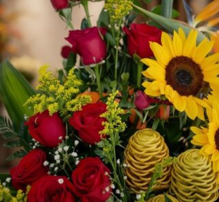Primer plano extremo de un arreglo floral con rosas rojas, girasoles amarillos vibrantes, flores de jengibre durio y pequeñas
