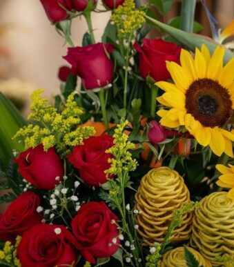 Primer plano extremo de un arreglo floral con rosas rojas, girasoles amarillos vibrantes, flores de jengibre durio y pequeñas