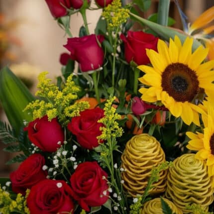 Primer plano extremo de un arreglo floral con rosas rojas, girasoles amarillos vibrantes, flores de jengibre durio y pequeñas