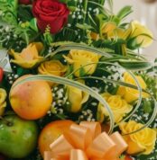 Primer plano extremo de un arreglo floral con rosas amarillas y rojas, manzanas verdes y naranjas, con sutiles gotas de rocío