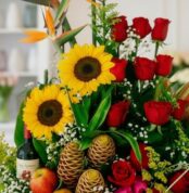 Primer plano extremo de un arreglo floral con girasoles, rosas rojas, frutas y una botella de vino, mostrando texturas hiperr