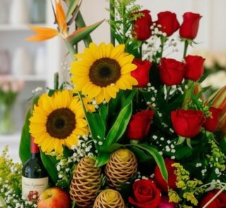 Primer plano extremo de un arreglo floral con girasoles, rosas rojas, frutas y una botella de vino, mostrando texturas hiperr