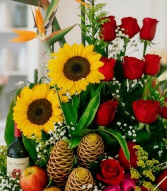 Primer plano extremo de un arreglo floral con girasoles, rosas rojas, frutas y una botella de vino, mostrando texturas hiperr