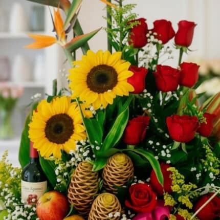 Primer plano extremo de un arreglo floral con girasoles, rosas rojas, frutas y una botella de vino, mostrando texturas hiperr