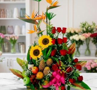 Arreglo floral con frutas y vino, girasoles, rosas rojas y aves del paraíso sobre mármol, estilo estudio premium.
