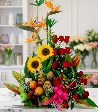 Arreglo floral con frutas y vino, girasoles, rosas rojas y aves del paraíso sobre mármol, estilo estudio premium.