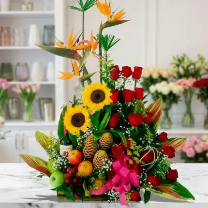 Arreglo floral con frutas y vino, girasoles, rosas rojas y aves del paraíso sobre mármol, estilo estudio premium.