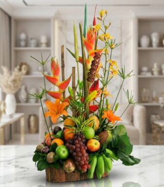 Arreglo floral con frutas exóticas, lirios naranjas, orquídeas amarillas y heliconias rojas, sobre base de madera rústica en