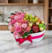 Arreglo floral en caja de corazón con rosas rosadas, alstroemerias, uvas, peras, manzanas y chocolates Ferrero Rocher sobre m