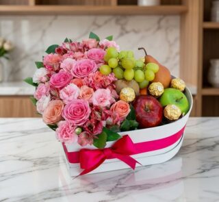 Arreglo floral en caja de corazón con rosas rosadas, alstroemerias, uvas, peras, manzanas y chocolates Ferrero Rocher sobre m