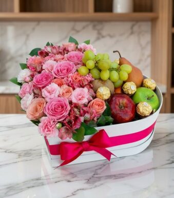 Arreglo floral en caja de corazón con rosas rosadas, alstroemerias, uvas, peras, manzanas y chocolates Ferrero Rocher sobre m