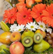 Primer plano extremo de Arreglo Floral con Frutas Hadar, mostrando gerberas naranjas, margaritas blancas, peras, kiwis, manza