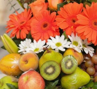 Primer plano extremo de Arreglo Floral con Frutas Hadar, mostrando gerberas naranjas, margaritas blancas, peras, kiwis, manza