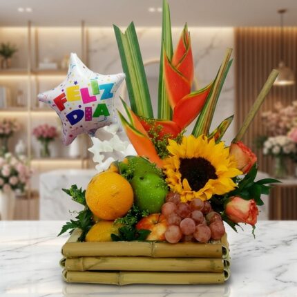 Arreglo floral frutero con tamarillos, uvas, naranjas, girasoles, rosas y heliconias, sobre mármol en floristería premium.