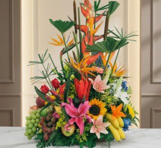 Arreglo floral con frutas exóticas, lirios, girasoles y aves del paraíso sobre mármol, ideal para floristería premium.