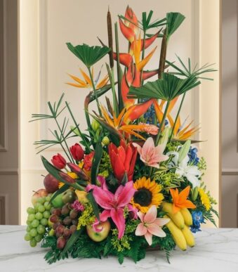 Arreglo floral con frutas exóticas, lirios, girasoles y aves del paraíso sobre mármol, ideal para floristería premium.