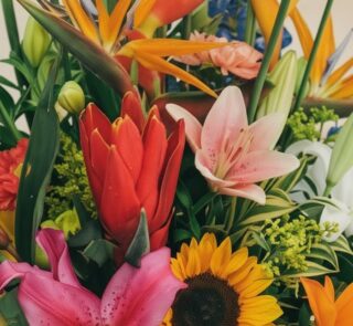 Primer plano extremo de un arreglo floral con lirios rosados, girasoles, aves del paraíso y flores rojas, mostrando texturas
