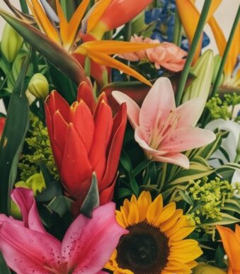 Primer plano extremo de un arreglo floral con lirios rosados, girasoles, aves del paraíso y flores rojas, mostrando texturas