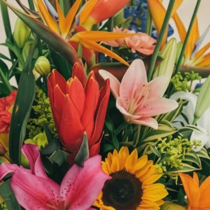 Primer plano extremo de un arreglo floral con lirios rosados, girasoles, aves del paraíso y flores rojas, mostrando texturas