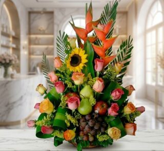 Arreglo floral con rosas de colores, girasoles, heliconias, uvas, peras y manzanas, sobre una superficie de mármol en un ento