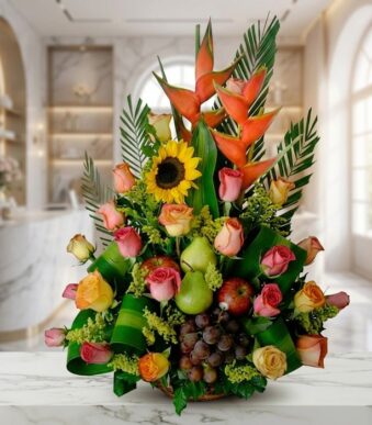 Arreglo floral con rosas de colores, girasoles, heliconias, uvas, peras y manzanas, sobre una superficie de mármol en un ento