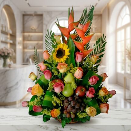 Arreglo floral con rosas de colores, girasoles, heliconias, uvas, peras y manzanas, sobre una superficie de mármol en un ento