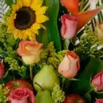 Primer plano extremo de un arreglo floral con girasoles, rosas de colores, peras verdes y manzanas rojas, destacando texturas