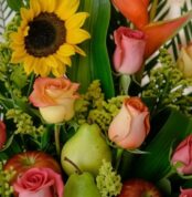 Primer plano extremo de un arreglo floral con girasoles, rosas de colores, peras verdes y manzanas rojas, destacando texturas