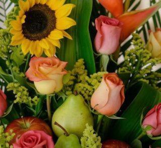 Primer plano extremo de un arreglo floral con girasoles, rosas de colores, peras verdes y manzanas rojas, destacando texturas