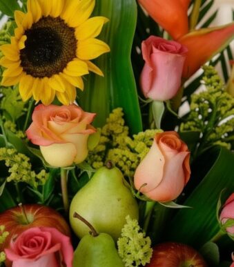 Primer plano extremo de un arreglo floral con girasoles, rosas de colores, peras verdes y manzanas rojas, destacando texturas