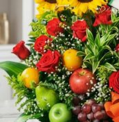 Primer plano extremo de Arreglo Floral con Frutas Trópico, mostrando rosas rojas, girasoles, naranjas, manzanas, peras y uvas