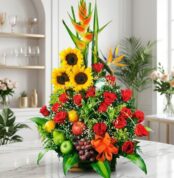 Arreglo floral grande y vibrante con girasoles, rosas rojas, heliconias, aves del paraíso y frutas tropicales frescas como ma