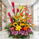 Arreglo floral exótico GINGER con orquídeas hawaianas, heliconias, girasoles y lirios en tonos vibrantes, sobre mármol.