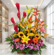 Arreglo floral exótico GINGER con orquídeas hawaianas, heliconias, girasoles y lirios en tonos vibrantes, sobre mármol.