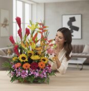 Mujer joven sonriente admirando un arreglo floral exótico GINGER con orquídeas hawaianas, heliconias, girasoles y ginger en u