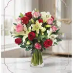 Arreglo floral GIORGIA con rosas rojas, rosas rosadas y lirios blancos en un jarrón de cristal, sobre una mesa de mármol con