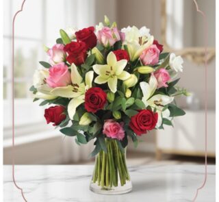 Arreglo floral GIORGIA con rosas rojas, rosas rosadas y lirios blancos en un jarrón de cristal, sobre una mesa de mármol con