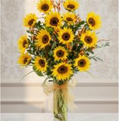 Arreglo floral de girasoles LENU en un jarrón de cristal con lazo dorado, sobre una mesa de mármol y fondo elegante.