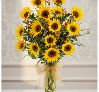 Arreglo floral de girasoles LENU en un jarrón de cristal con lazo dorado, sobre una mesa de mármol y fondo elegante.