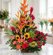 Arreglo floral IDARA exótico y vibrante con rosas rojas, girasoles, lirios y aves del paraíso, sobre mármol en floristería pr