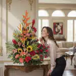 Mujer elegante admirando con deleite el Arreglo Floral IDARA, un diseño exclusivo con rosas y flores exóticas en un lujoso in