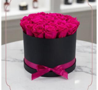 Arreglo Floral Marena con 21 rosas fucsia vibrantes y frescas en una caja redonda negra con lazo fucsia, sobre una mesa de má