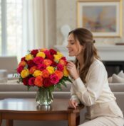 Mujer joven y elegante admirando y oliendo un Arreglo Floral MARIELLA con 36 rosas frescas multicolor (rojas, amarillas, nara