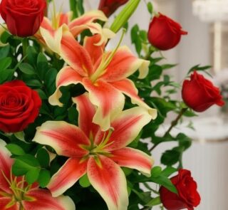 Primer plano extremo de un arreglo floral 'Me Encantas' con lirios bicolores y rosas rojas, mostrando texturas hiperrealistas