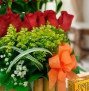 Primer plano extremo de Arreglo Floral Musca con rosas rojas, follaje verde, gotas de rocío y lazo naranja, destacando textur